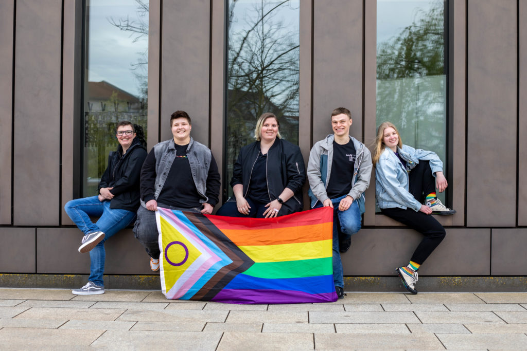 Hier sieht man die Vorstandschaft des CSD Reutlingen e.V., mit einer Progress Flagge in der Hand vor der Stadthalle in Reutlingen.